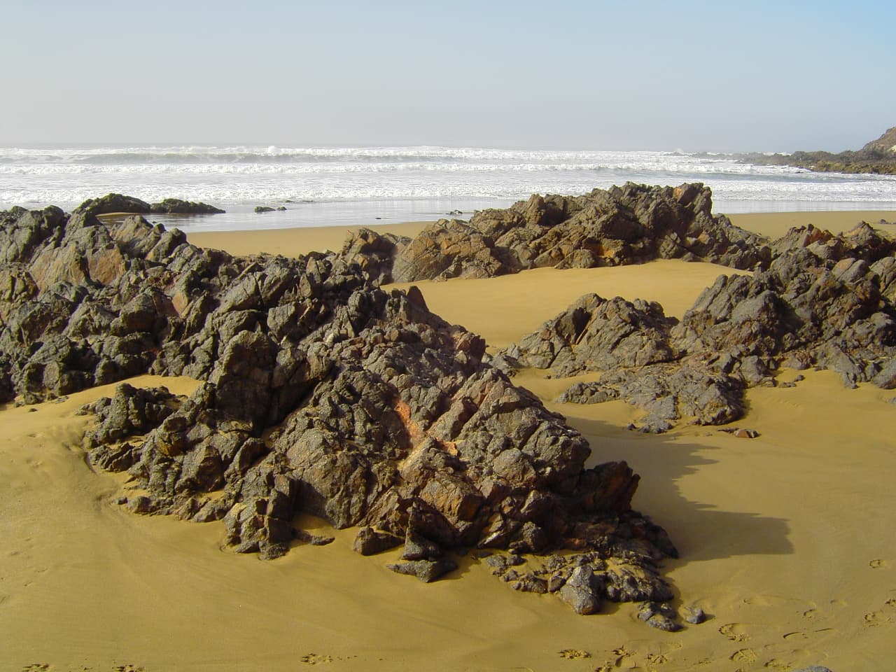Rochers sombres et sable doré sur une plage sauvage au sud d'Aglou, sur la côte de Tiznit